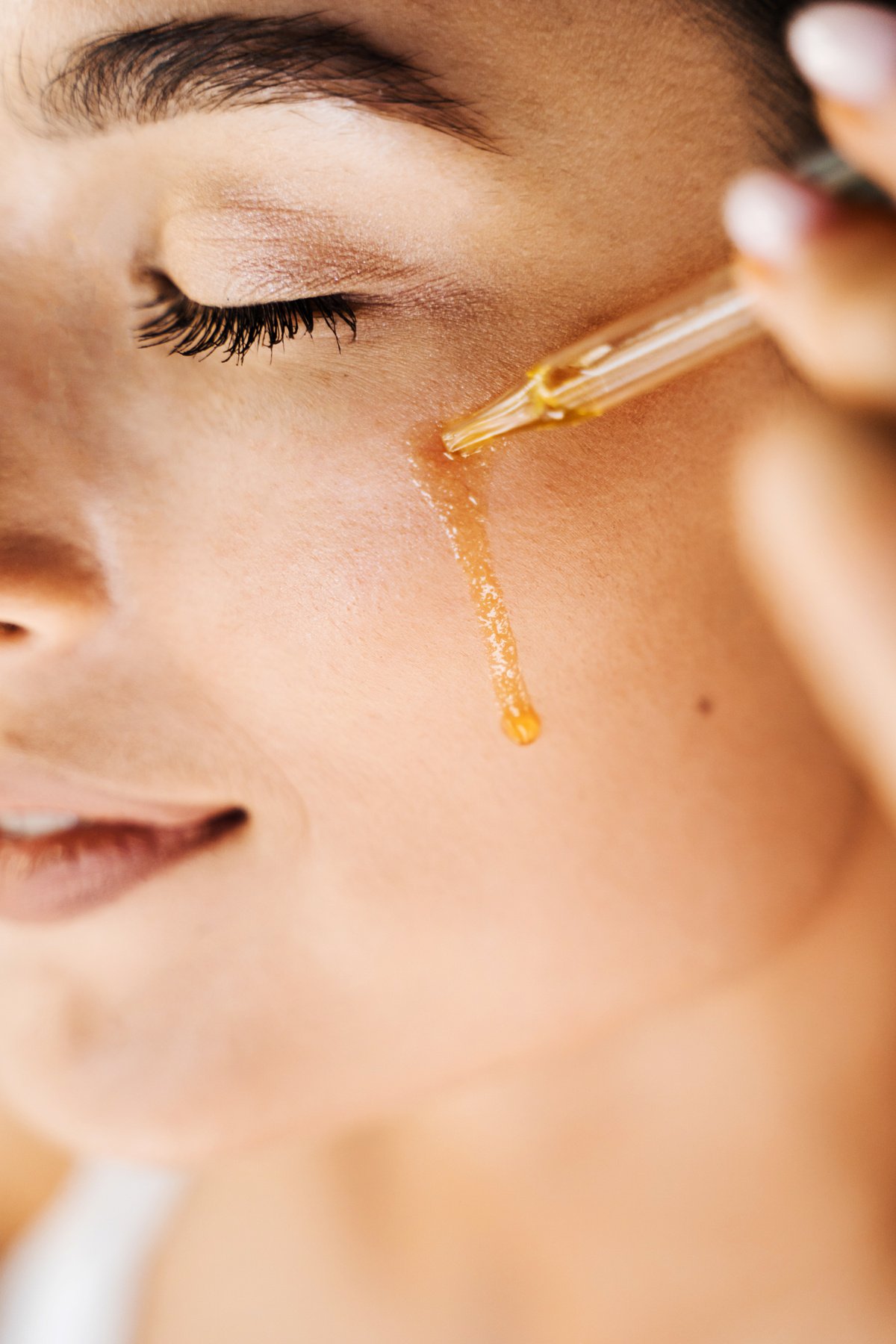 Girl is dropping hyaluronic acid or serum from pipette on face close-up. Young woman is applying moisturizing serum on her face.